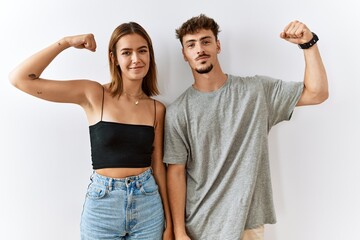 Wall Mural - Young beautiful couple standing together over isolated background strong person showing arm muscle, confident and proud of power