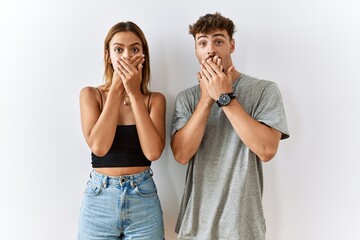 Wall Mural - Young beautiful couple standing together over isolated background shocked covering mouth with hands for mistake. secret concept.