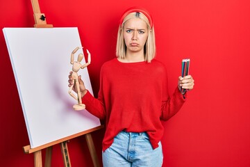 Poster - Beautiful blonde woman holding small wooden manikin and pencils depressed and worry for distress, crying angry and afraid. sad expression.