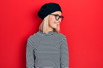 Poster - Beautiful blonde woman wearing french look with beret an glasses looking away to side with smile on face, natural expression. laughing confident.