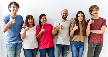 Poster - Group of young friends standing together over isolated background doing happy thumbs up gesture with hand. approving expression looking at the camera showing success.