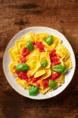 Wall Mural - Ravioli with tomato sauce and fresh basil on a plate. Healthy Italian meal, shot from above on a dark rustic wooden background