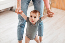 Little Baby Boy Or Girl Taking First Steps With Mother Help, Woman Holding Child's Hands, Home Interior, Closeup
