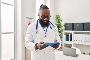 Poster - Young african american man wearing doctor uniform using touchpad at clinic