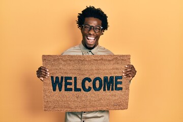 Sticker - Young african american man holding welcome doormat smiling and laughing hard out loud because funny crazy joke.