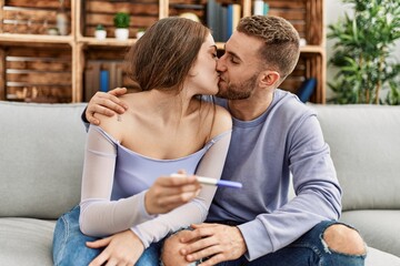 Wall Mural - Young caucasian couple kissing and holding pregnant test at home.