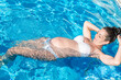 © Diego - young smiling pregnant woman in white bikini swimming in the pool while on vacation. sports, exercises and relaxation during pregnancy for health care.