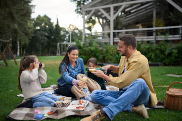 Wall Mural - Happy young family sitting on blanket and having take away picnic outdoors in restaurant area.