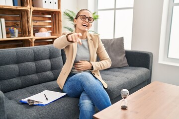 Wall Mural - Young woman working at consultation office laughing at you, pointing finger to the camera with hand over body, shame expression