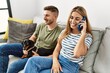 © Krakenimages.com - Young hispanic couple smiling happy talking on the smartphone sitting on the sofa with dog at home.