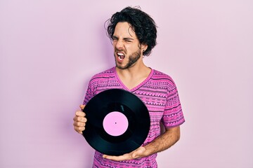 Sticker - Handsome hispanic man holding vinyl disc angry and mad screaming frustrated and furious, shouting with anger. rage and aggressive concept.