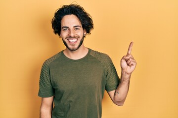 Wall Mural - Handsome hispanic man wearing casual green t shirt smiling with an idea or question pointing finger up with happy face, number one