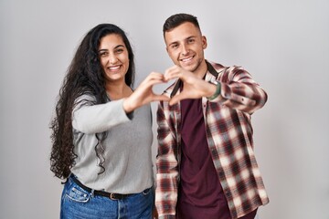 Wall Mural - Young hispanic couple standing over white background smiling in love doing heart symbol shape with hands. romantic concept.