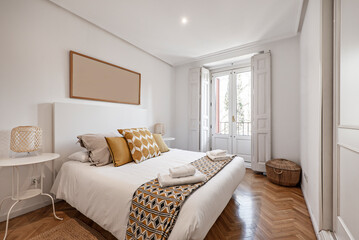  Double bedroom with bed with white duvet, matching blanket and cushions, white with wooden windows and herringbone oak flooring