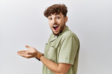 Wall Mural - Young arab doctor man standing over isolated background pointing aside with hands open palms showing copy space, presenting advertisement smiling excited happy