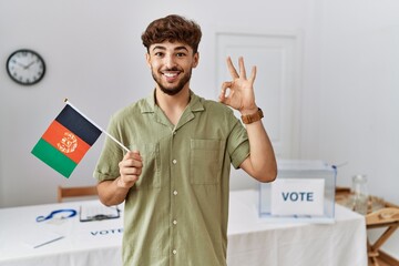 Sticker - Young arab man at political campaign election holding afghanistan flag doing ok sign with fingers, smiling friendly gesturing excellent symbol