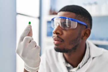 Sticker - Young african american man wearing scientist uniform holding pill at laboratory