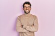 Handsome man with beard wearing turtleneck sweater and glasses happy face smiling with crossed arms looking at the camera. positive person.