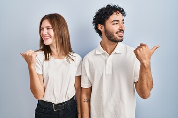 Canvas Print - Young couple wearing casual clothes standing together smiling with happy face looking and pointing to the side with thumb up.