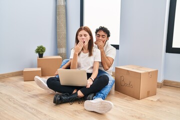 Poster - Young couple using laptop at new home bored yawning tired covering mouth with hand. restless and sleepiness.