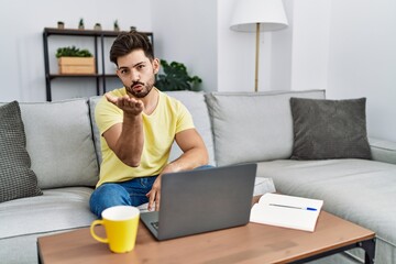 Poster - Young man with beard using laptop at home looking at the camera blowing a kiss with hand on air being lovely and sexy. love expression.