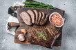 Roast and sliced tri tip beef steak on a wooden board with herbs. Gray background. Top view