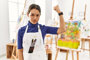 Sticker - Young brunette woman at art studio strong person showing arm muscle, confident and proud of power