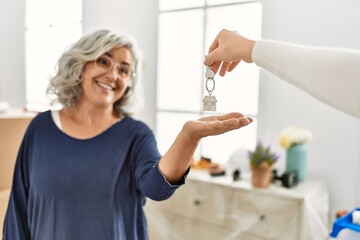 Sticker - Middle age grey-haired woman smiling happy holding key of new home.