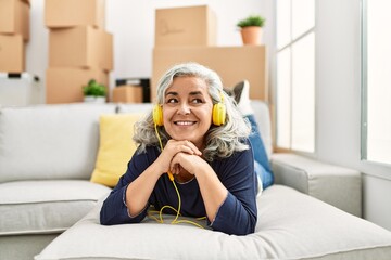 Poster - Middle age grey-haired woman listening to music lying on the sofa at new home.