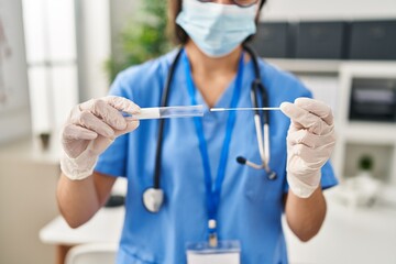 Young hispanic woman wearing doctor uniform holding covid-19 pcr test at clinic