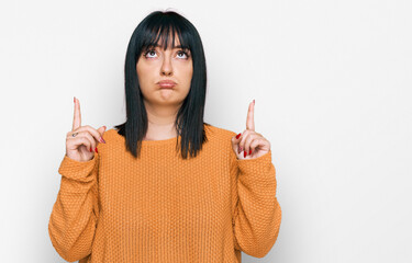 Canvas Print - Young hispanic woman wearing casual clothes pointing up looking sad and upset, indicating direction with fingers, unhappy and depressed.