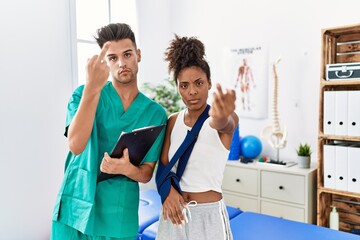 Canvas Print - Physiotherapist working with patient wearing arm on sling at rehabilitation clinic showing middle finger, impolite and rude fuck off expression