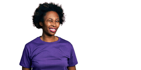 Poster - African american woman with afro hair wearing casual purple t shirt winking looking at the camera with sexy expression, cheerful and happy face.