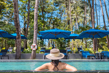 Happy Asian Woman In Red Swimsuit And A Straw Hat Relaxing In Swimming Pool Looking At View By The Pool At Koh Mak, Phangnga, Thailand. Relax And Travel Concept. Comfort Resort Summer Vacation