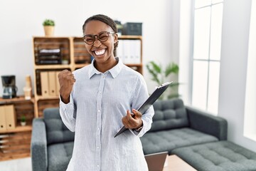 Wall Mural - African woman working at psychology clinic very happy and excited doing winner gesture with arms raised, smiling and screaming for success. celebration concept.