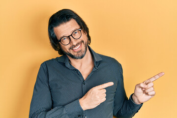 Canvas Print - Middle age caucasian man wearing casual clothes and glasses smiling and looking at the camera pointing with two hands and fingers to the side.