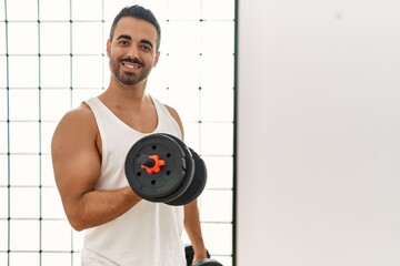 Sticker - Young hispanic man smiling confident training using dumbbells at sport center