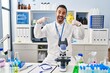 © Krakenimages.com - Young hispanic man with beard working at scientist laboratory smiling cheerful showing and pointing with fingers teeth and mouth. dental health concept.