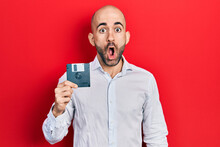 Young Bald Man Holding Floppy Disk Scared And Amazed With Open Mouth For Surprise, Disbelief Face