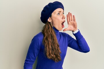 Canvas Print - Young blonde woman wearing french look with beret shouting and screaming loud to side with hand on mouth. communication concept.