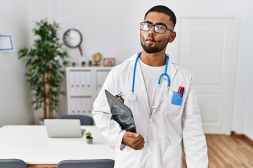 Sticker - Young indian man wearing doctor uniform and stethoscope making fish face with lips, crazy and comical gesture. funny expression.