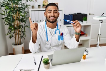 Poster - Young indian doctor holding thermometer smiling happy pointing with hand and finger to the side