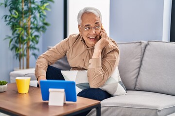 Sticker - Senior man talking on the smartphone watching touchpad at home