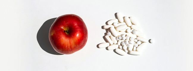 Red apple and pills or vitamin capsules on white table, copy space. Wellness, diet or supports for health concept.