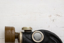 Side View Of A Black Rubber Gas Mask On A White Wooden Background. Close Up Of Old Army Gas Mask With Filter