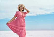 Laughing Emotionally Woman In Pink Dress And Hat Carefree And Happy On Blue Sky White Salt Beach Landscape. Feeling Freedom