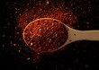 Spicy chili pepper flakes, crushed, milled dry paprika pile in wooden spoon isolated on black, top view