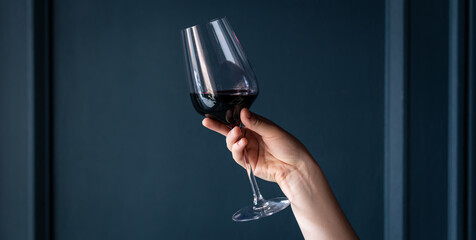 Wall Mural - A glass of red wine in a female hand on a blue background.