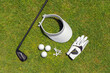 Top view of golf equipment on green grass on a golf course. Flat lay of golf club, balls, glove, tees and cap