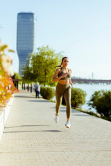 Wall Mural - Young woman taking running exercise by the river promenade